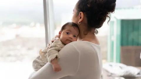 Getty Images A mother holds her baby upright to rest on her shoulder