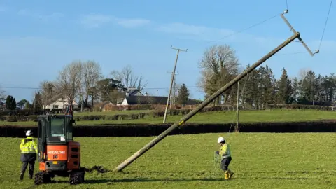 A power line fallen on its side in a field. Two workers are on either side and a forklift is on the left.