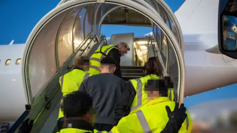 Home Office A man being led onto a plane by staff in hi-vis jackets