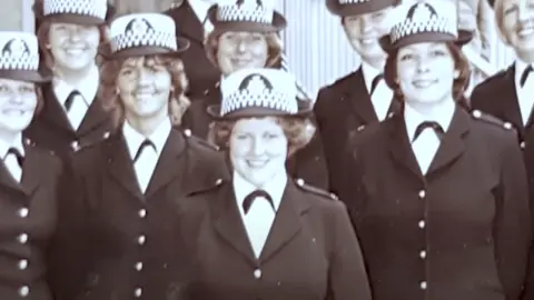 Avon and Somerset Police A black and white photo of eight female police officers in smart uniform. They are all smiling and standing shoulder to shoulder.