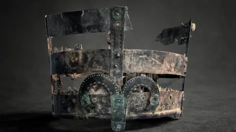 Discover Bucks Museum Close up of the upside down remains of a metal fame of a Saxon drinking bucket. It has two and a half circular bands of metal held together with uprights. The lower level has snake necked monster decorations. 