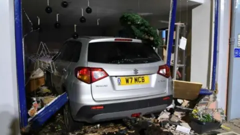 Crown Office A rear view of a silver car which has smashed through an office window leaving debris all around