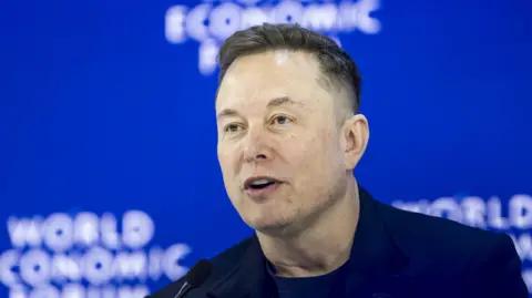EPA A file picture of Elon Musk wearing a dark suit and a dark T-shirt, speaking in front of a bright blue background with the logo of the World Economic Forum in Davos.