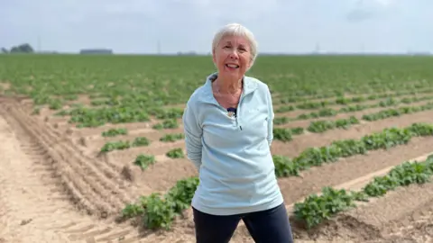 A woman is standing in a field with a crop growing in the soil behind her
