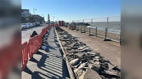 A seafront path in Herne Bay which has been cordoned off with red, plastic barriers. Half the pavement is torn up.