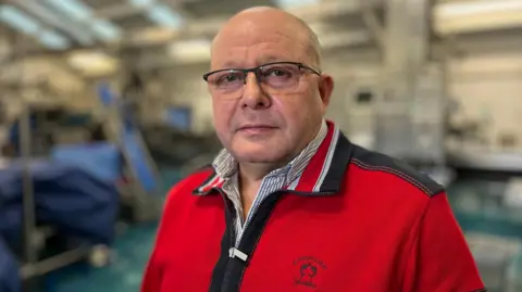 Martin Giles/BBC Steve Williamson wearing glasses and a red top standing in his shellfish factory.