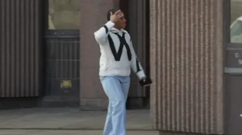 BBC Image shows Elizabeth Adeagbo outside Liverpool Crown Court. She is wearing blue jeans and a white top with a large W in black on the front of it. 