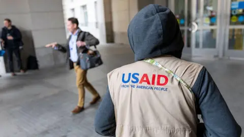 EPA A worker wearing an USAID vest is seen walking near a building 