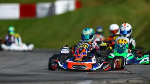 Supplied Jack, with a blue helmet on, is driving his kart with number 291on it. Four karts are following behind.