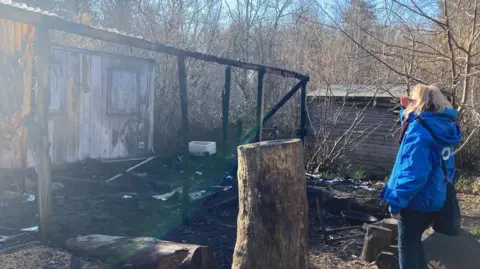 A woman looking over to a badly burnt wooden structure.