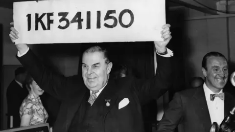 Getty Images Lord Mackintosh of Halifax holds aloft the first winning number of the £1,000, 1KF341150