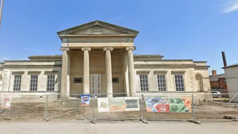 A grand Georgian-style building sitting behind temporary fencing. 