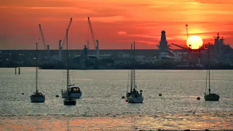 Alison Treacher Boats are on the water below a sky painted red by the setting sun.