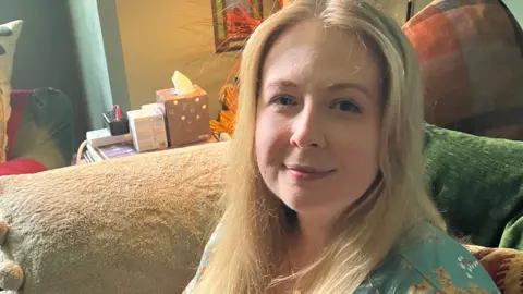 Erin Sullivan, a young woman, with long blonde hair, sitting on a sofa, smiling at the camera