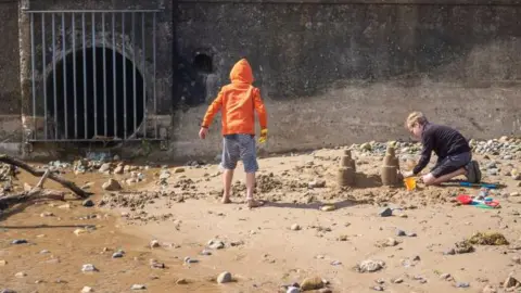 Getty Images Two children build sand castles next to a storm drain outlet.