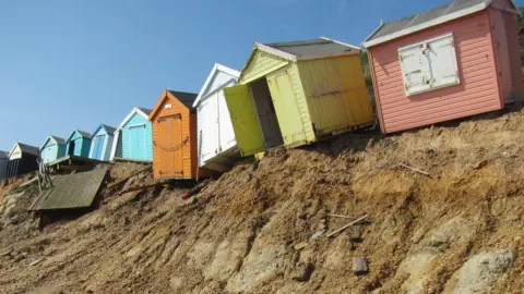 New Forest District Council Looking up from the beach at the huts coloured from left to right... blue, turquoise, orange, white, yellow and salmon pink