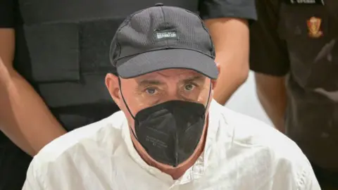 Getty Images A man wearing a white shirt, a black cap and a black face mask