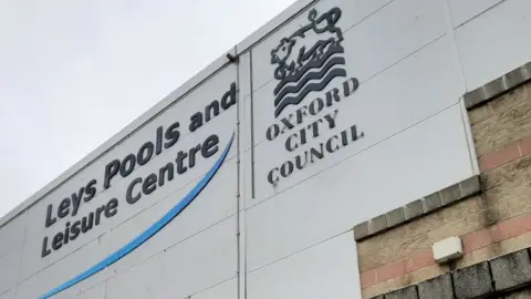 Words on the side of a white building say "Leys Pools and Leisure Centre" and "Oxford City Council"