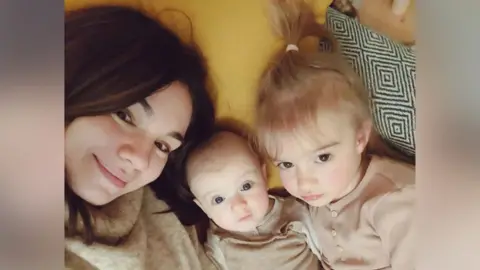 Judy Morgan A mum smiles at the camera with her two young children