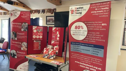 Stephen Huntley/BBC A booth that has been set up within a rugby clubhouse providing information about cardiac risk in the young. There are large information boards that stand either side of a table. There are information leaflets resting on the table.