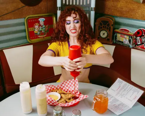 Ryan Lee Clemens Chappelle Rowan, on the set of the Hot To Go video, squeezes ketchup into a basket of fried chicken, in a typical American restaurant