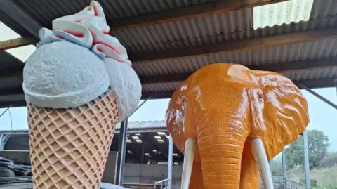 Rob Taverner A giant ice cream cone statue next to a large orange elephant statue stood in a barn on a Devon farm