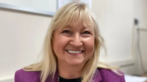 Harry Parkhill/ BBC A head and shoulders shot of Council leader Anne Dorrian. She is wearing a black top and a purple blazer. She has blonde long hair and is smiling at the camera. 