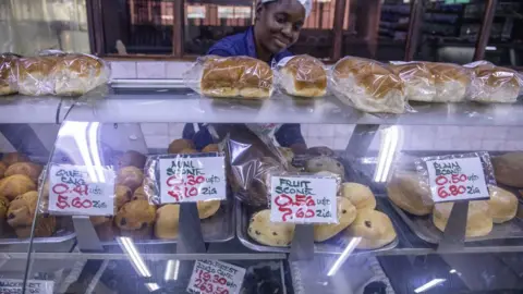 Getty Images A supermarket worker at a bakery counter, where the prices are shown in US dollars and Zimbabwean Zigs, Harare, Zimbabwe - 30 April 2024
