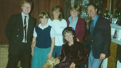 PA Media A grainy, aged, colour photo of Suzy, her brother, her two sisters and her parents. 
