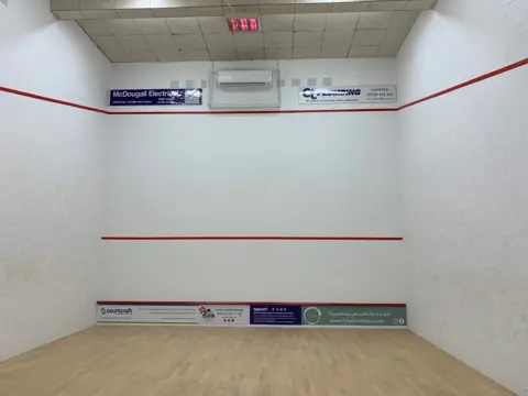 A squash court with white walls and two red stripes and a wooden floor