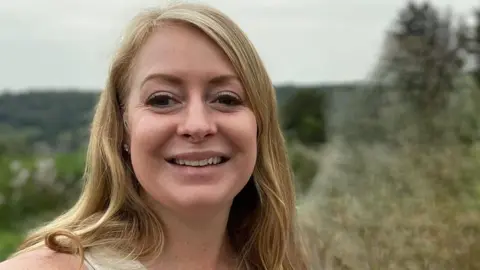 Jennifer Symonds has long blonde hair and dark eyes. The picture is a selfie.