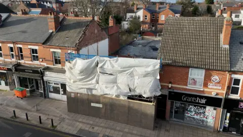 BBC A drone image showing a row of properties - the aerial shot shows that two buildings in the middle of the terraced street have been demolished. Scaffolding covers the front of where the buildings were.