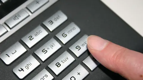 A person's finger hovering over the nine button on a telephone dial pad.