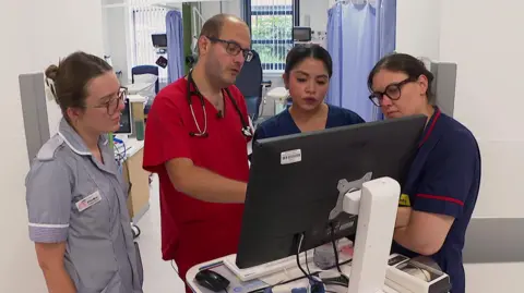 Four doctors/nurses stood looking at a screen at the Royal Devon and Exeter Hospital.