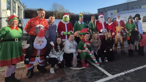 A group of people in an industrial estate car park wearing Christmas costumes.