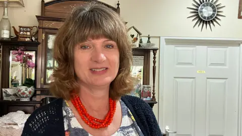 GUY CAMPBELL/BBC Woman wearing bright red bead necklace stands in a shop