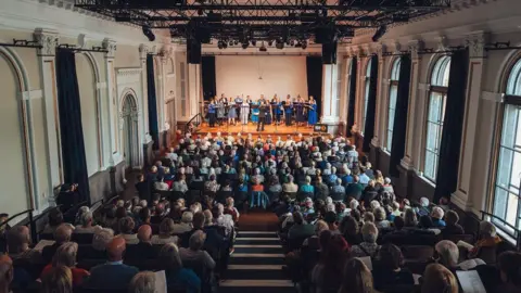 Guilia Spadafora/Soul Media Hundreds of people are seated watching the BBC singers perform on the stage in The Lantern at Bristol Beacon. The photograph is taken from the back of the auditorium