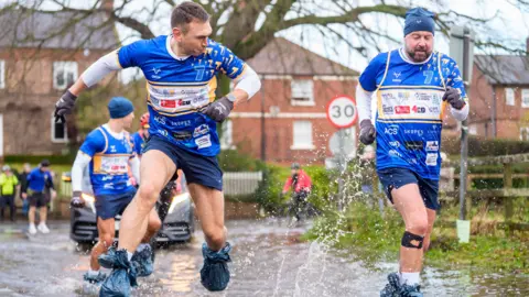Danny Lawson/PA Wire Kevin Sinfield sporting bin bags to cover his footwear as he runs through flood water in Cattal.