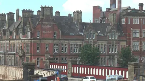 Exterior of the red brick Lancashire County Council HQ with red and white panelled bridge in front of it.