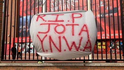 Marc Gaier/BBC A sheet reads R.I.P JOTA Y.N.W.A on the metal fence outside Anfield