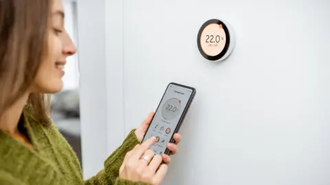 Getty Images A woman interacts with the Google Nest smart thermostat on a wall