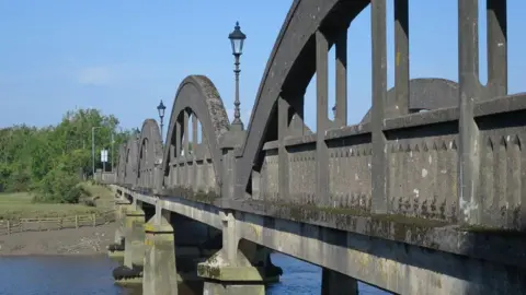 Dave Croker/Geograph sebuah jembatan yang terbentang di seberang sungai, dipandang dekat dari samping. Itu terbuat dari beton dan memiliki lumut tumbuh di atasnya