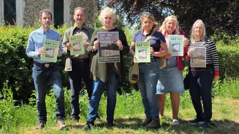 We can see four women and two men standing outside a church holding up signs which say "Say No To The Rushall Bess"
