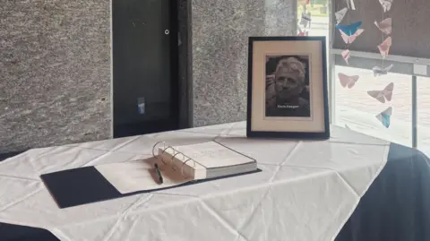 A black and white framed photograph of Kevin Keegan sits on a white tablecloth next to the open book of condolence at Newcastle Civic Centre.