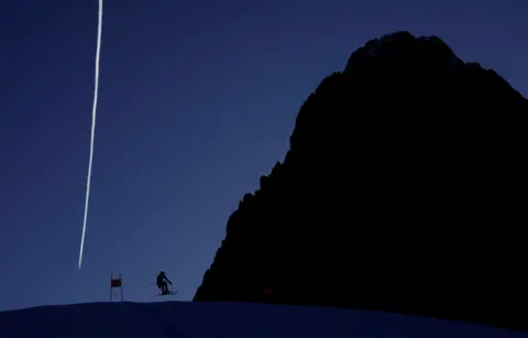 Leonhard Foeger/Reuters Skier Kyle Negomir is silhouetted against the scenery  and bluish  entity  arsenic  helium  practises a skis  tally  astatine  Val Gardena, successful  Italy. He appears tiny   beside a elephantine  rock, which is besides  successful  silhouette, portion    a achromatic  vapour way   stands successful  the entity  down  them both. 