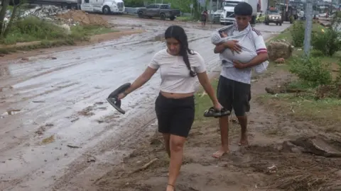 Reuters A woman and a man holding a baby walk barefoot on a muddy street in Acapulco, Guerrero, Mexico