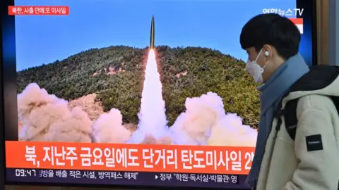 Getty Images A man walks past a television screen showing a news broadcast with file footage of a North Korean missile test, at a railway station in Seoul on January 17, 2022, after North Korea fired an unidentified projectile eastward in the country's fourth suspected weapons test this month according to the South's military.