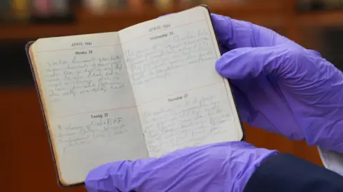PA Media A curator wearing purple gloves holds Vera Lynn's personal diary detailing her 1944 tour of India. The pages have handwritten entries for each day and there are two days per page. The diary is open, showing entries for the 24 to 27 April 1944.