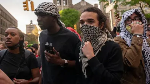 Protesters wearing keffiyeh headscarves and masks outside Butler Library