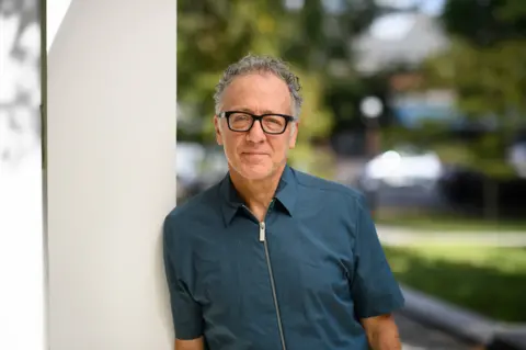 Professor Thomas Levin Professor Thomas Levine has short grey hair and is wearing thick black glasses. He is wearing a zipped blue shirt and is pictured leaning against a post outside with greenery in the background